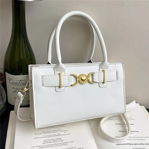 Elegante borsa a mano bianca quadrata con fibbia a cuore dorata presentata su un libro