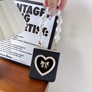 Chic black leather phone bag with pearl handle and golden bow heart detail on a desk