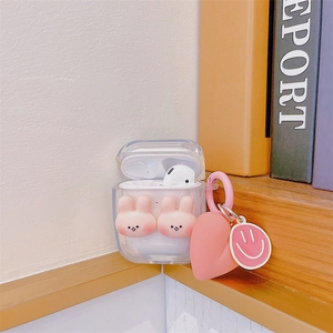 Clear AirPods case featuring 3D pink rabbits and heart charm on a wooden shelf