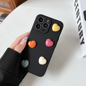 Custodia iPhone nera opaca con cuori 3D colorati tenuta in mano su sfondo minimal