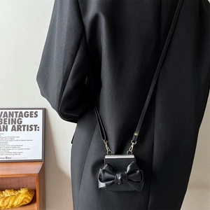 Detail of black crossbody case featuring a large leather bow and delicate shoulder strap