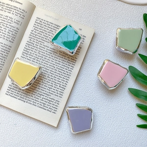 Set of colorful macaron enamel brooches with silver edges on a white textured background