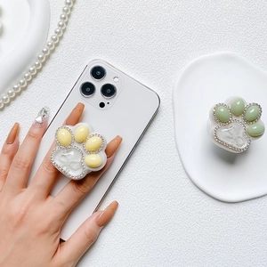 Cute cat paw phone grip with rhinestones and pearl details on a clean white desk