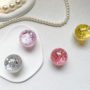 Detailed view of four glitter phone grips in pink, silver, red, and yellow on pearls