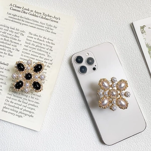 Luxurious rhinestone phone grip with floral metal frame and pearl inlay on a white smartphone