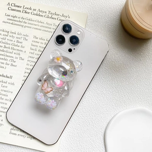 Close-up of a bear-shaped transparent glitter phone grip with butterfly and flower inserts