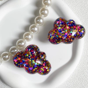 Detail of colorful sequins inside cloud-shaped resin hair clips on a white plate