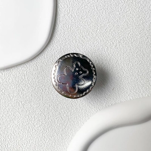 Macro shot of silver metallic phone grip featuring a cute bear relief on a white surface