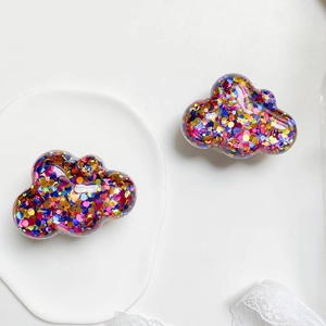 Detail of transparent cloud hair clip with colorful sequins on white ceramic plate