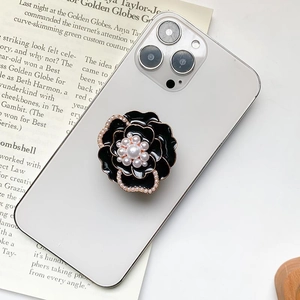 Detailed view of luxury black camellia flower phone grip with pearls on white smartphone