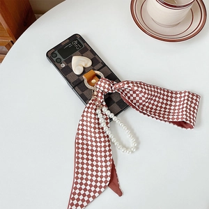 Detail of checkered Z Flip 3 case with heart decor, pearl chain and silk ribbon bow