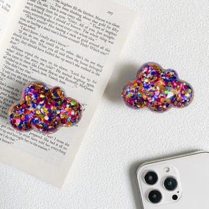 Cloud-shaped phone grip with colorful sequins on a desk with a white smartphone