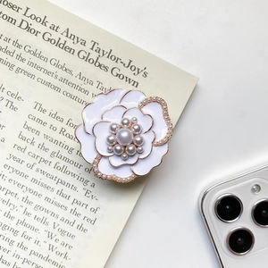 Detailed view of luxury metal pearl flower phone grip stand on a white smartphone