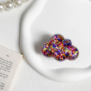 Macro shot of cloud-shaped phone grip with multi-color sequins on white porcelain tray