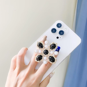 Luxurious cross-shaped phone grip with black gemstones and pearls on a white smartphone