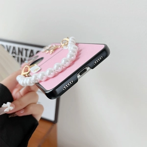 Detail view of pink textured phone case with pearl strap and gold heart charm