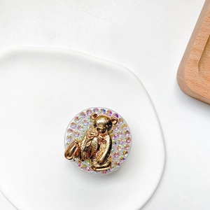 Macro view of a gold 3D bear phone grip with colorful rhinestones on a ceramic tray