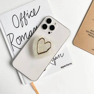 Minimalist cream heart-shaped phone grip stand with gold trim on a white mobile phone
