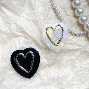 Close-up of minimalist heart phone grip accessories in black and pearl white with gold trim