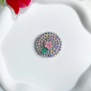 Close-up of a round rhinestone phone grip with a pink flower on a ceramic tray