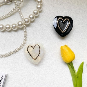 Detail of heart-shaped marble phone grip in black and pearl white with golden metallic rim