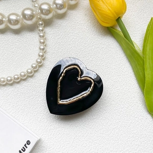 Detailed view of a glossy black heart hair clip with gold metal rim and retro chic style