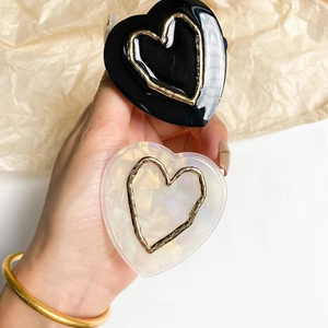 Detailed view of glossy black and pearl white heart-shaped phone grips with gold metal trim