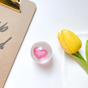 Pink heart-shaped crystal grip tok phone stand shown with a yellow tulip on white background