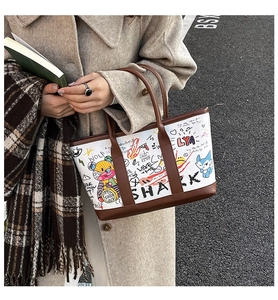 Close-up of a white tote bag featuring artistic graffiti and brown leather handles in detail