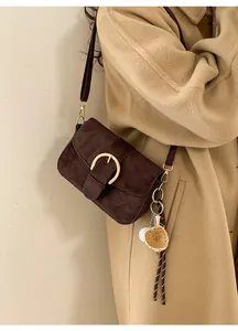 Detail of vintage brown suede crossbody bag featuring a large gold buckle and sports charm