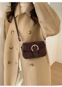 Detailed view of dark brown suede shoulder bag with a round gold metal buckle on a beige coat