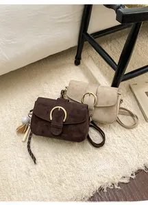 Detail of suede crossbody bag with large metal ring buckle and sports themed charms