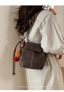 Dettaglio borsa a secchiello marrone vintage con cuciture a contrasto e ciondoli pompon