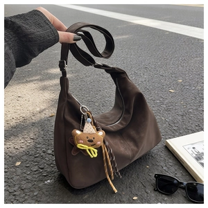 Detail of dark brown suede hobo bag with cute bear charm and tassel on asphalt background