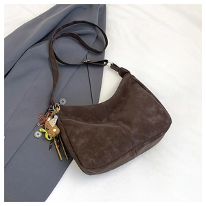 Detail of dark brown suede crescent bag with adjustable strap and cute bear charm