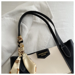 Detail of contrast stitching leather handle and decorative scarf on a tote bag