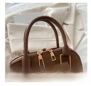 Detail view of suede shell bag featuring brown leather handle and gold metal hardware
