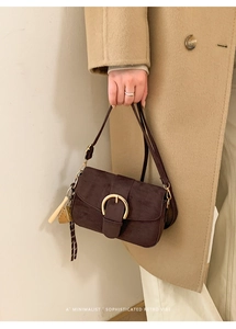 Close-up of retro brown suede underarm bag with gold horseshoe buckle and wooden charm