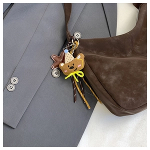 Detail of a plush bear charm with beige polka dot hat on a dark brown hobo bag