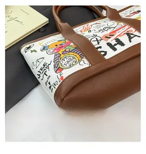 Detail view of stitched brown leather bottom and graffiti canvas on a tote bag