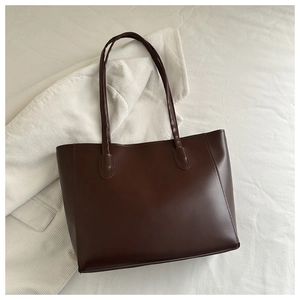 Detail of dark brown tote bag with smooth faux leather texture and slender shoulder straps