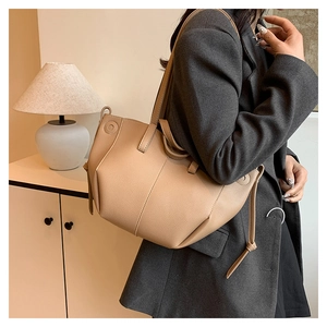 Minimalistische beige Schultertasche aus Leder an Model mit grauem Blazer getragen