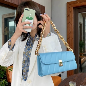 Close-up of sky blue quilted shoulder bag with chunky gold chain strap and metal lock