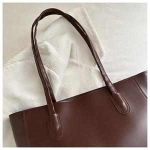 Detail of dark brown tote bag showing matte leather texture and reinforced stitching