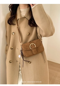 Detail of retro dark brown suede crossbody bag with gold round buckle and baseball charm