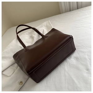 Close-up of a vintage dark brown tote bag showing smooth PU leather and fine stitching detail