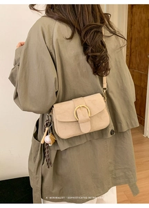Close-up of beige suede crossbody bag with gold buckle and baseball charm detail