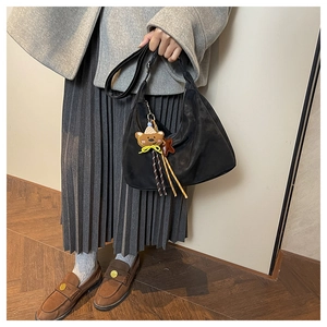 Detail of black suede crescent bag featuring a cute bear charm and woven rope accent