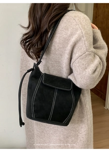 Dettaglio di borsa a secchiello nera con cuciture a contrasto sulla spalla di una modella