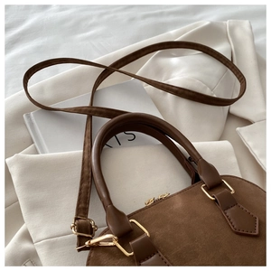 Detailed close-up of dark brown suede-textured handbag with gold hardware and leather handles